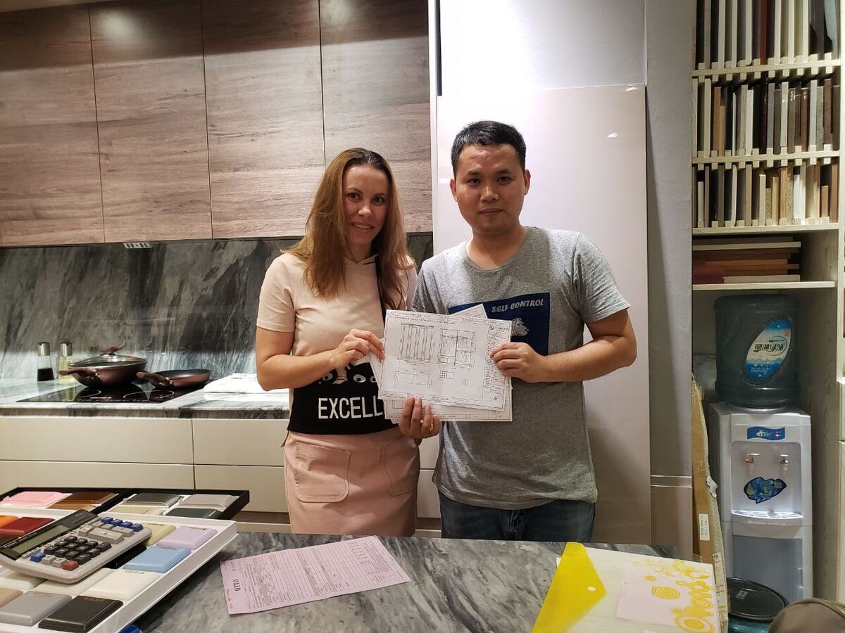 Екатерина и китайский менеджер оформляют заказ на кухню: в руках чертёж, на столе образцы и калькулятор